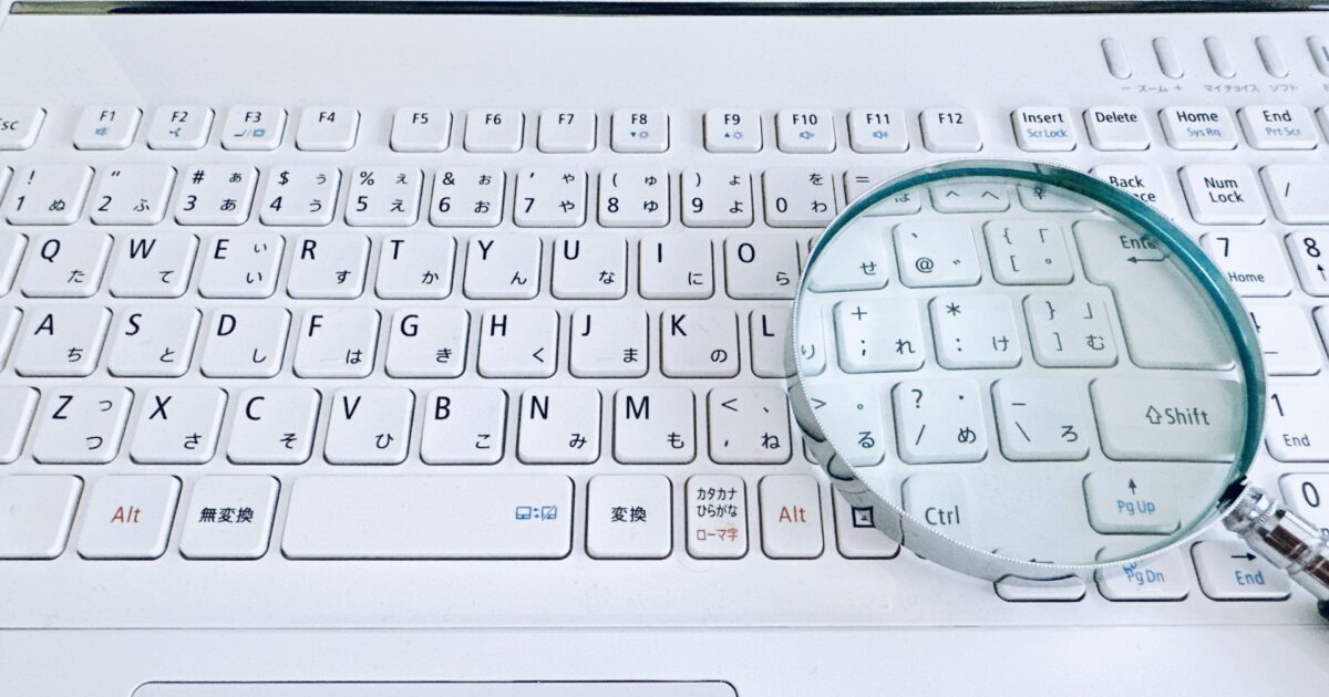 白いノートパソコンのキーボードと虫眼鏡のクローズアップ